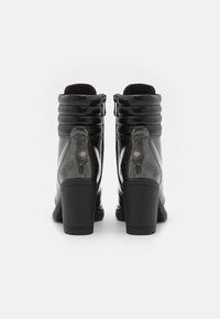 Botas de tobillo de cuero negro con un puño acolchado, acabado brillante y tacones en bloque. Presentan un cierre con cremallera lateral y una suela texturizada para mayor tracción.