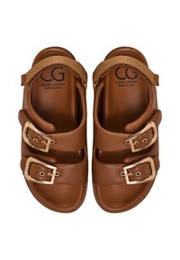 Een paar bruine leren sandalen met elk twee gouden gespen en een verstelbare stoffen band aan de achterkant, van binnen gebrandmerkt met Cesare Gaspari Barcelona.
