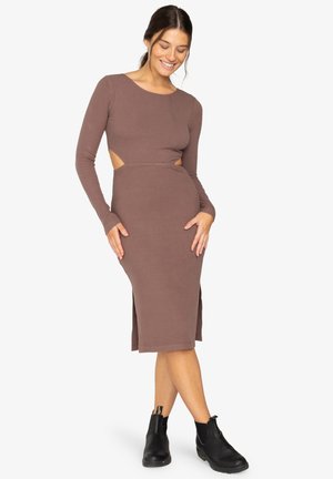 Robe marron à manches longues et côtelées avec des découpes sur les côtés, longueur au genou et silhouette ajustée, associée à des bottines noires à la cheville.