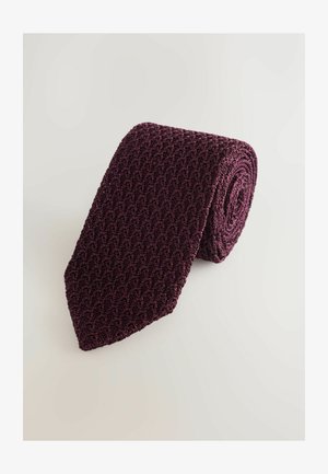 Bordowy, dziergany krawat z teksturowanym wzorem, zwinięty i nachylony, by ukazać jego trójkątny czubek, wykonany z miękkiego, elastycznego materiału.