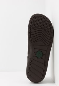 Braune Gummisohle mit strukturierten Profilmustern, ausgestattet mit einem kreisförmigen Logoabdruck und einer Größenangabe von 44 an der Seite.