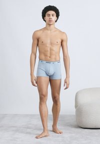 Ανοιχτό μπλε βαμβακερό μπόξερ με μαύρο λογότυπο Nike στη ζώνη, σχεδιασμένο να είναι εφαρμοστό και με ομαλή υφή, φορεμένο από έναν όρθιο μοντέλο.