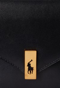 Borsa in pelle nera con una chiusura rettangolare dorata e un emblema di un giocatore di polo nero. Texture liscia con bordi cuciti.