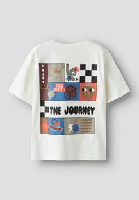 T-shirt blanc avec des blocs graphiques colorés incluant une tasse de café, un crayon, un visage souriant, le texte "TU L'AS FAIT !" et la phrase "LE VOYAGE".