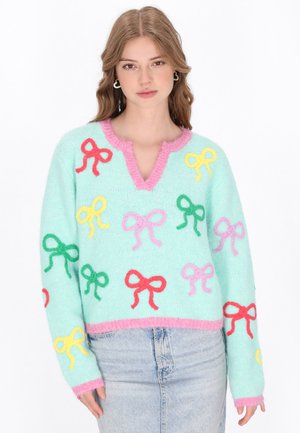 Pull en tricot vert menthe avec un col en forme de volant rose. Il présente des nœuds brodés multicolores en rouge, jaune, vert et rose. Coupe courte.