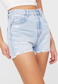 Shorts in denim azzurro chiaro con dettagli strappati, vita alta, orli sfilacciati e design a cinque tasche standard. Realizzati in tessuto di cotone.