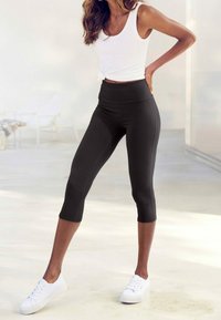 Svarta capri leggings med hög midja, tillverkade av stretchigt tyg, matchade med en vit ärmklippt topp och vita sneakers.