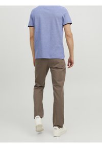 Pánský outfit s modrou košilí s krátkým rukávem a hnědými kalhotami, doplněný bílými teniskami. Košile má základní střih; kalhoty jsou zúžené a mají kapsy.