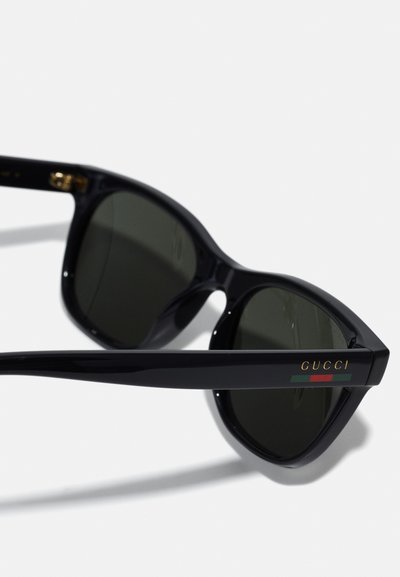 Gucci prillid musta plastraami, nurkse kujunduse, tumedate objektiivide ja kuldse logoga küljes, mis sisaldab punase ja rohelise tooni aktsente.
