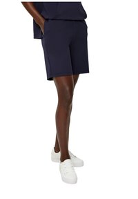 Marineblaue Shorts aus weichem Stoff, mit seitlichen Taschen, leicht über Knie-länge, kombiniert mit weißen Sneakern.