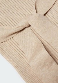Tessuto a coste beige con dettaglio della cintura annodata. La texture è morbida e liscia, con linee verticali che creano una profondità sottile.