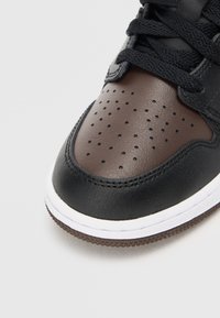 Tenis din piele neagră și maro, cu vârf perforat, șireturi plate negre, talpă din cauciuc și talpă intermediară albă. Accente texturate pe material.