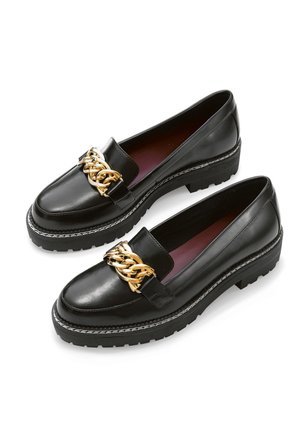 Sorte læder loafers med chunky såler og stor guldkæde detalje henover toppen, vist side om side på en hvid baggrund.