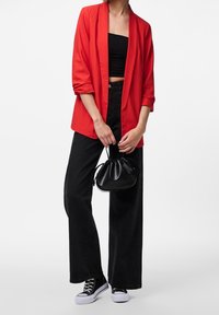 Červené sako, černý krátký top, černé kalhoty s vysokým pasem a širokými nohavicemi, a černé tenisky. Malá černá kabelka dodává outfitu kontrast.