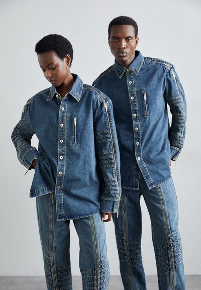Chemises en denim avec fermetures à bouton et poches zippées. Les pantalons présentent des détails cousus, le tout dans un délavage bleu clair. Conception à coupe décontractée.