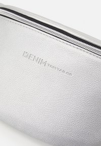 Zbliżenie na srebrną, teksturowaną sakiewkę z czarnym zamkiem błyskawicznym i wytłoczonym na przodzie logo "DENIM TOM TAILOR".