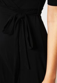 Musta kangasmekko, jossa on solmittava vyötäröyksityiskohta, sileä pinta, lyhyet hihat ja vartalonmyötäinen leikkaus.