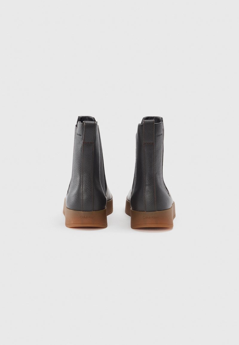 Schwarze Lederknöchelstiefel mit einer strukturierten Oberfläche, kontrastierenden braunen Gummisohlen und seitlichen Reißverschlüssen. Mit dezenter Markenkennzeichnung an der Ferse.