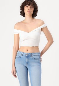 Bela obleka s spušenimi rameni in nabrano robom ter zavitim sprednjim delom, v kombinaciji s svetlo modrimi oprijetimi kavbojkami. Gladek občutek blaga.