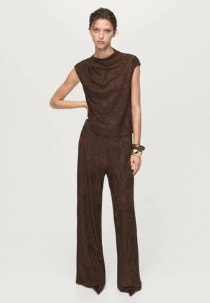 Jumpsuit marrone a fantasia floreale con maniche corte, vestibilità ampia e tessuto testurizzato. Presenta un girocollo alto e un design a gamba larga.