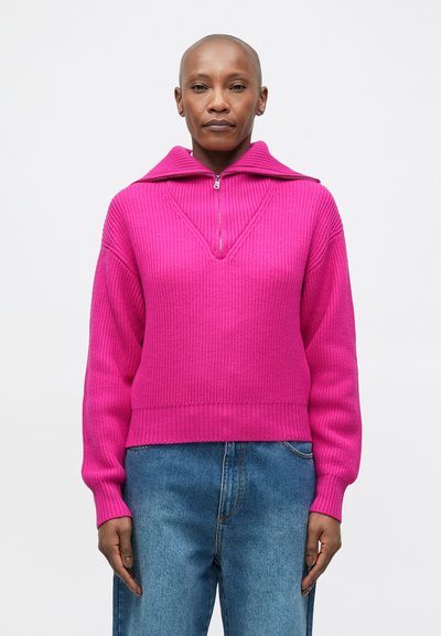 Pull en ribbée rose avec un col en V et un détail zip, doté d'un large col et d'une taille ajustée, associé à un jean en denim bleu clair.