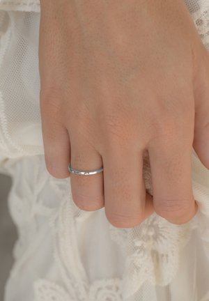 Silberring mit einer glatten, polierten Oberfläche, getragen an einer Hand vor einem strukturierten weißen Stoffhintergrund mit Spitzenverzierungen.