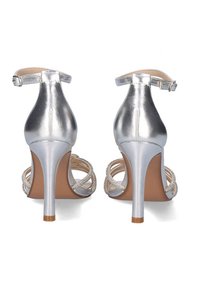 Sandalias de tacón alto metálicas plateadas con correas en el tobillo, parte trasera abierta y detalles de cuentas en un diseño de múltiples correas. Textura suave y punta afilada.