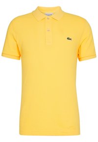 Žluté polo tričko vyrobené z texturované tkaniny, s límečkem a třemi knoflíky, na hrudi s malým zeleným logem krokodýla.