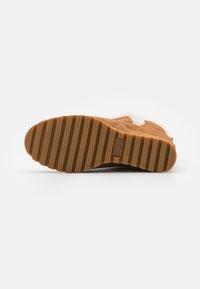 Botte en daim beige avec une épaisse doublure en fourrure blanche, dotée d'une semelle en caoutchouc brun texturé avec des rainures horizontales et un logo en relief.