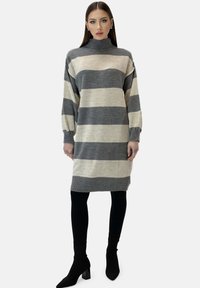 Randig klänning i grått och krämfärgat, har högt halsband, ballongsärmar samt ribbade muddar och fåll. Matchad med svarta leggings och klackar.