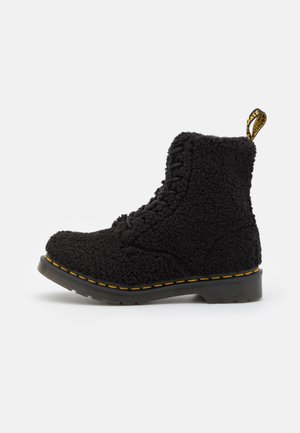 Bottine noire à lacets avec extérieur en polaire texturée, surpiqûres jaunes sur la semelle et languette de traction de marque à l’arrière.