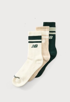 Tre par ribstrikkede New Balance crew-strømper i hvid, beige og mørkegrøn, hver med striber og brandlogo nær toppen.