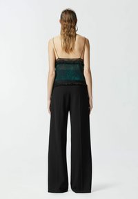 Crne široke hlače uparené s prilagođenim, prozirnim teal topom s čipkastim rubom i suptilnim uzorcima životinja.