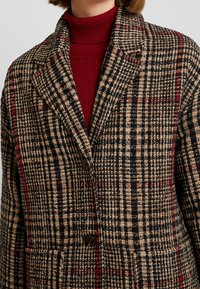 Blazer a quadri nei toni di marrone, nero e rosso, con un design doppiopetto, rever alette e tasche frontali con una finitura in tessuto texture.