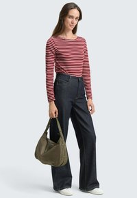 Rood-witte gestreepte longsleeve top gecombineerd met donkerblauwe wijde spijkerbroeken, terwijl ze een groene schoudertas vasthoudt, met witte sneakers.