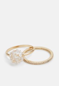 Trois anneaux en or : l'un présente un centre en cristal clair et facetté ; un autre a un bandeau lisse, et le troisième est orné de petites pierres.