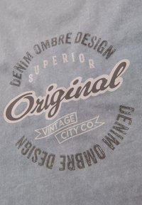 Šedá látka se zakulaceným logem designu s texty "DENIM OMBRE DESIGN", "ORIGINAL" a "VINTAGE CITY CO." v různých písmách a velikostech.