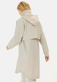 Helle beige wasserdichte Jacke mit Kapuze, hohem Kragen und elastischen Bündchen. Verfügt über eine lockere Passform und Rückenschlitze.