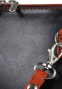 Schwarze Lederhandtasche mit strukturierter Oberfläche, braunem Riemen und silberner Hardware, mit Reißverschluss und detaillierter Nahtverarbeitung.