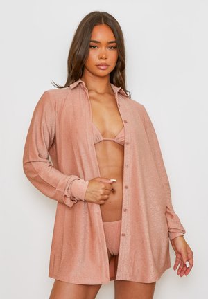 Jasnoróżowa, błyszcząca, oversize'owa koszula z długimi rękawami i zapięciem na guziki. Noszona na dopasowany bikini. Gładka tekstura, casualowy styl.