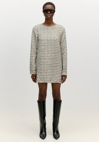 Witte en zwarte geruite mini-jurk met lange mouwen, rafelige zoom, gecombineerd met zwarte leren laarzen tot de knie en zwarte zonnebril.