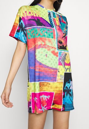 Mujer que lleva un vestido de manga corta de colores vivos con estampados vibrantes de temática hawaiana que incluyen surfistas, delfines, palmeras y puestas de sol.