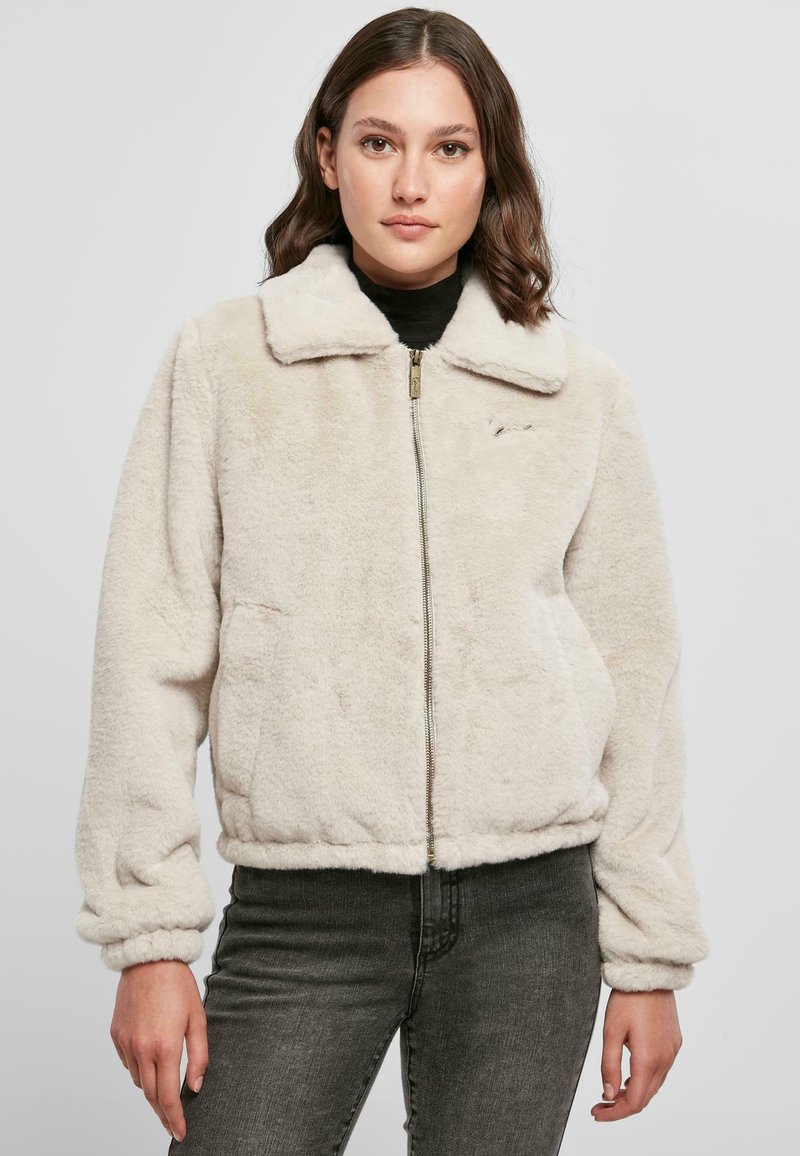 Faux fur zip-up jakke i creme; har krave, ribbede manchetter og to sidelommer. Tekstureret overflade med en blød fornemmelse.