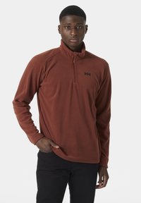 Polarowy pulower w kolorze spalonej pomarańczy z kołnierzem na zamek błyskawiczny do połowy i czarnym logo. Miękka faktura, długie rękawy oraz luźny krój.