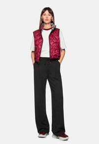 Quilted burgundy vest over a white t-shirt, paired with black pants and red-accented sneakers. The vest has a leopard-print collar.