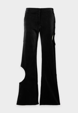 Mujer con el cabello largo y liso que lleva una blusa negra sin mangas y pantalones anchos con cortes en las rodillas, sosteniendo un bolso negro en el hombro.