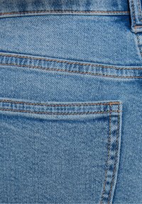 Ljusblå denimtyg med en bakficka som har kontrasterande orange söm och en mjuk textur. Designen är enkel och funktionell.