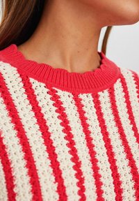 Czerwono-kremowy sweter w paski z falbaniastym dekoltem. Dziane wykończenie; naprzemienne poziome linie w jednolitym i otwartym wzorze. 