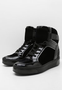 Černé vysoké tenisky s lesklými a matnými panely, tkaničkovým zapínáním, polstrovaným límcem a silnými gumovými podrážkami.