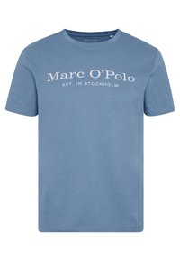 Camiseta de color azul claro hecha de algodón, con cuello redondo y mangas cortas. El texto frontal dice "Marc O'Polo EST. EN ESTOCOLMO" en blanco.